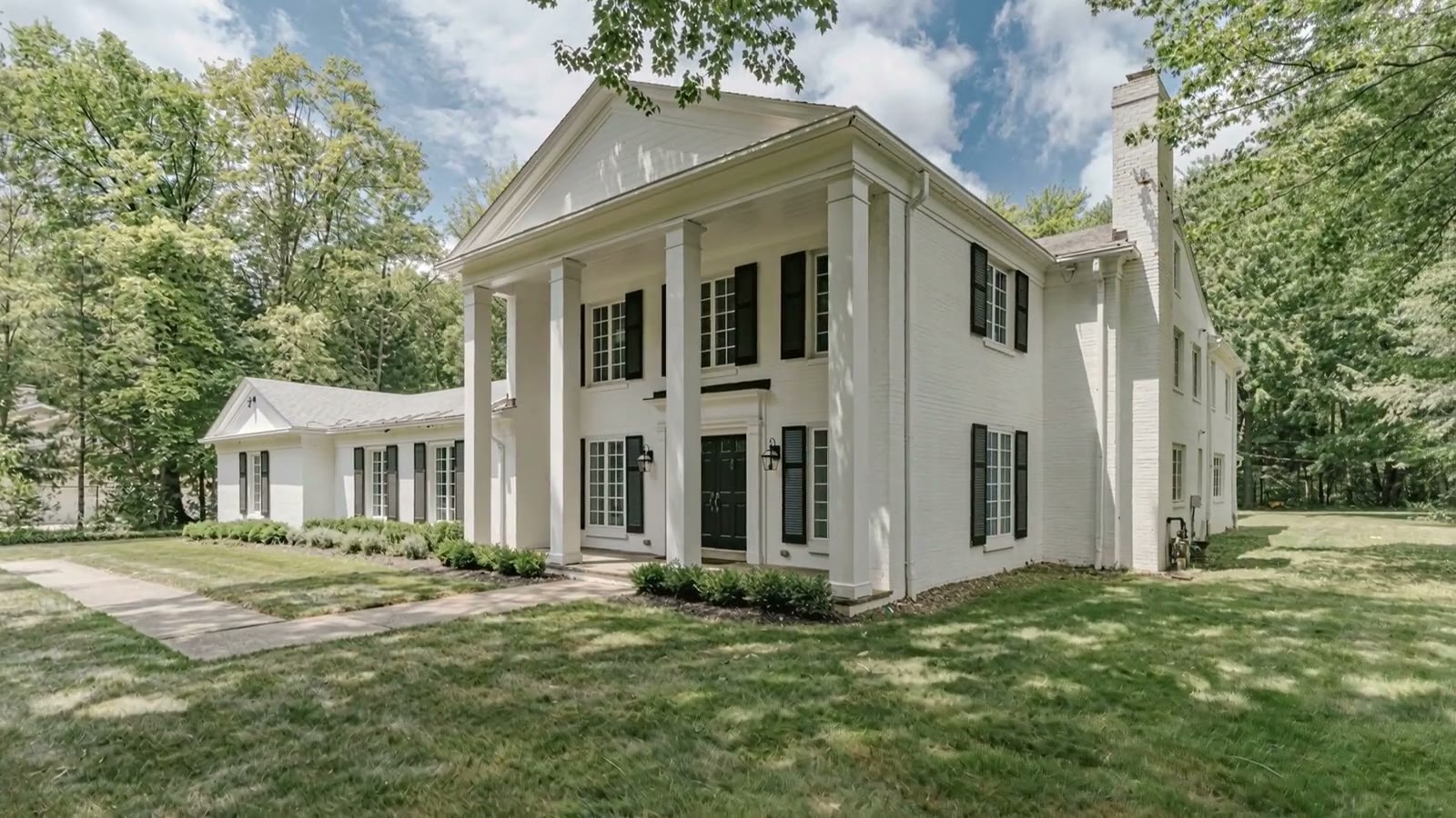 A white Greek Revival home with paired columns, seen from the drive